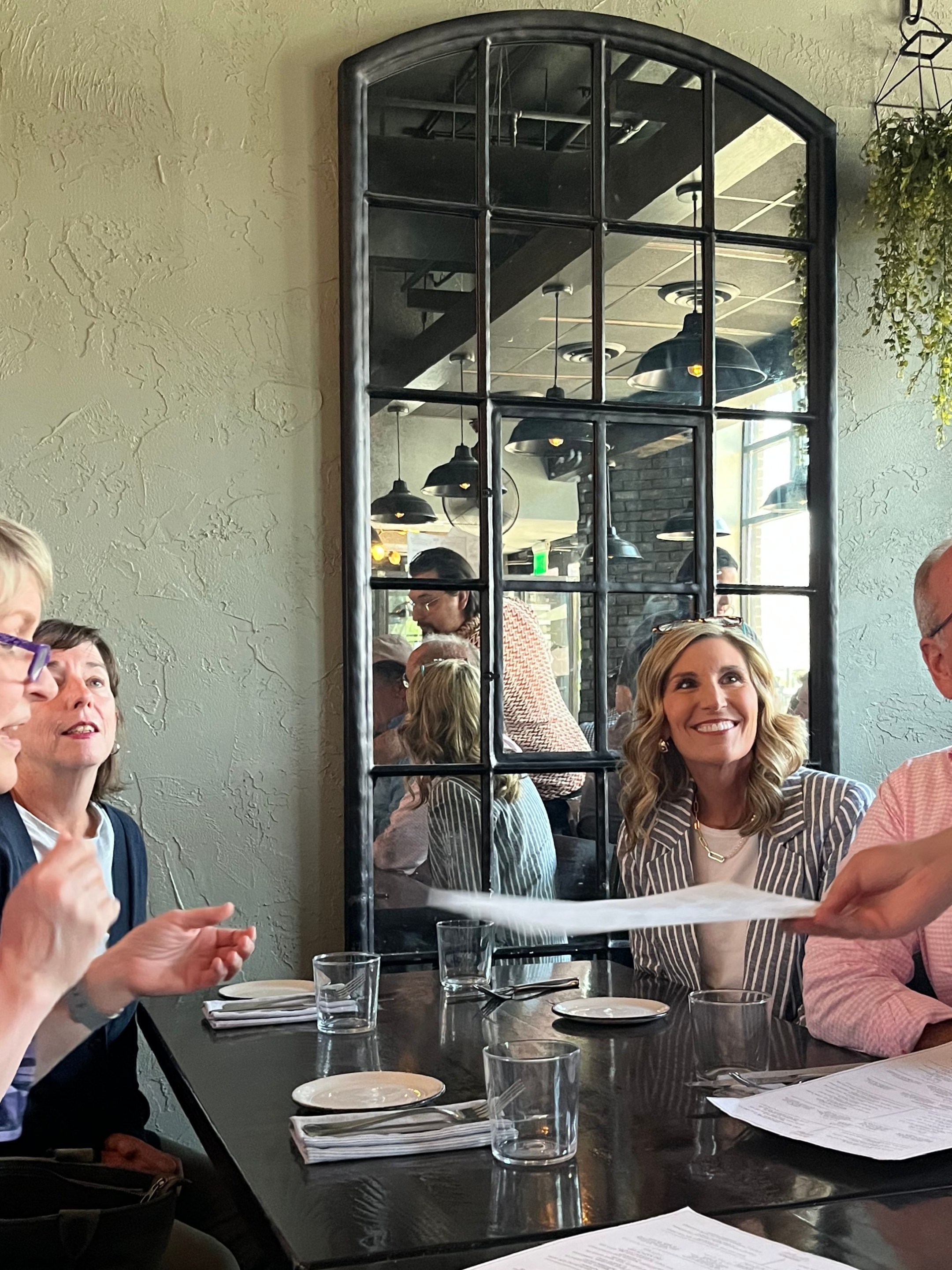 Group of four people talking and smiling at a restaurant table with menus.