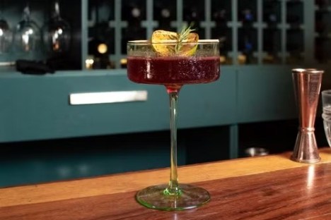 Cocktail glass with a dark drink and garnish on a wood bar.