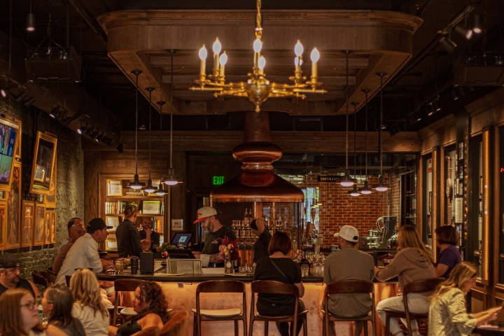 Cozy bar with patrons seated, warm lighting, and a chandelier above.