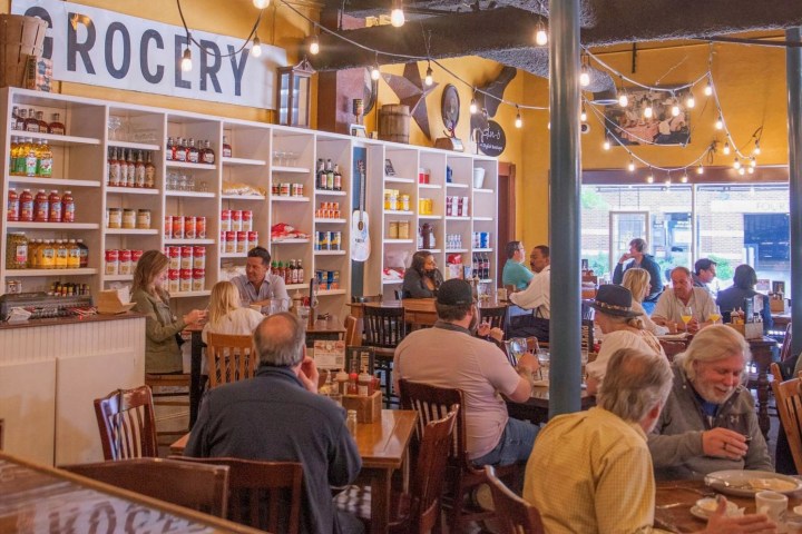People dining in a restaurant with grocery shelves and string lights.