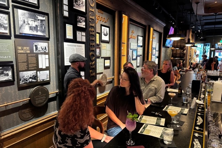 People seated at a bar in a dimly lit space with framed pictures on the wall.