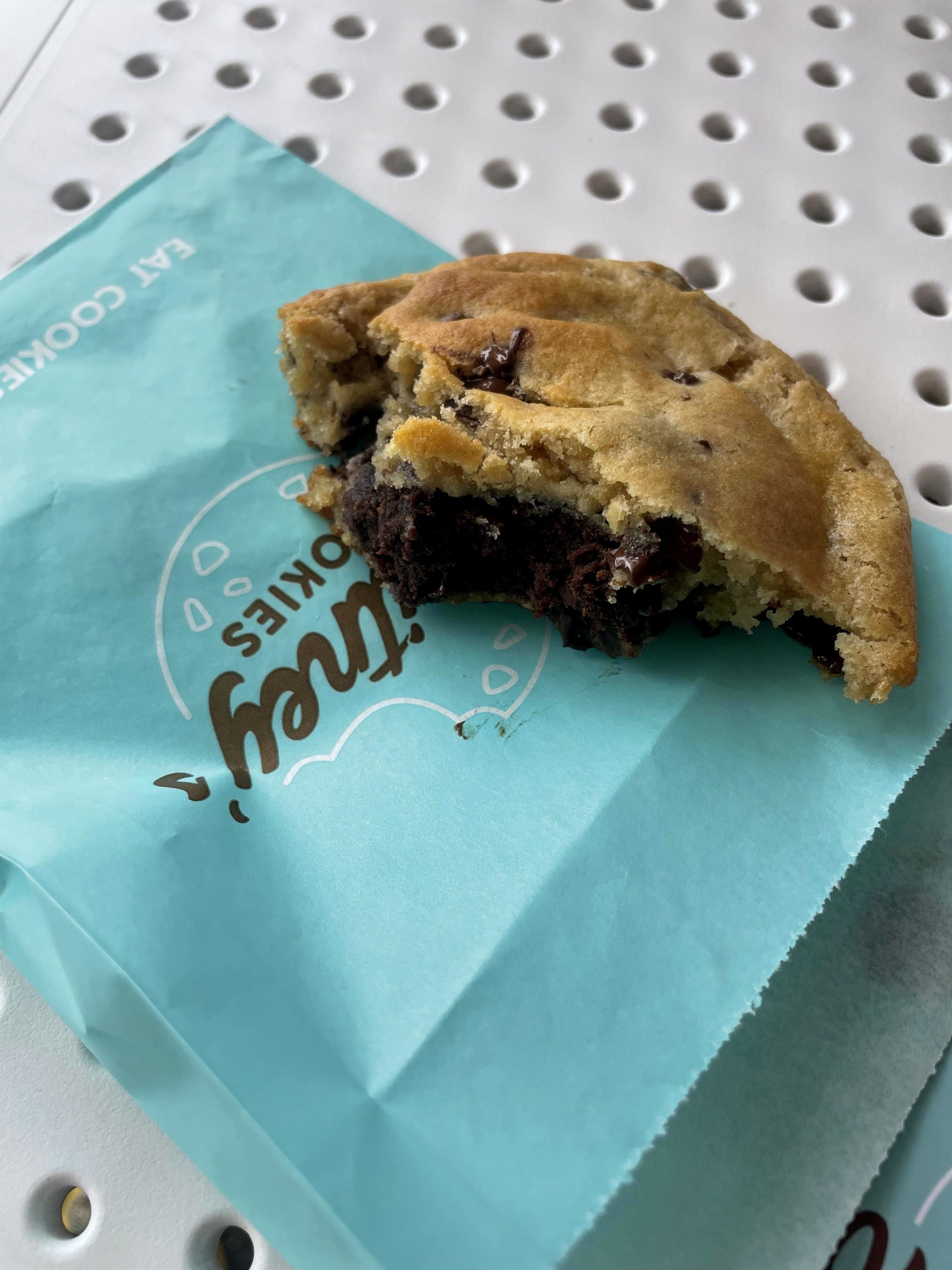 Partially eaten chocolate chip cookie on blue wrapper with perforated table background.