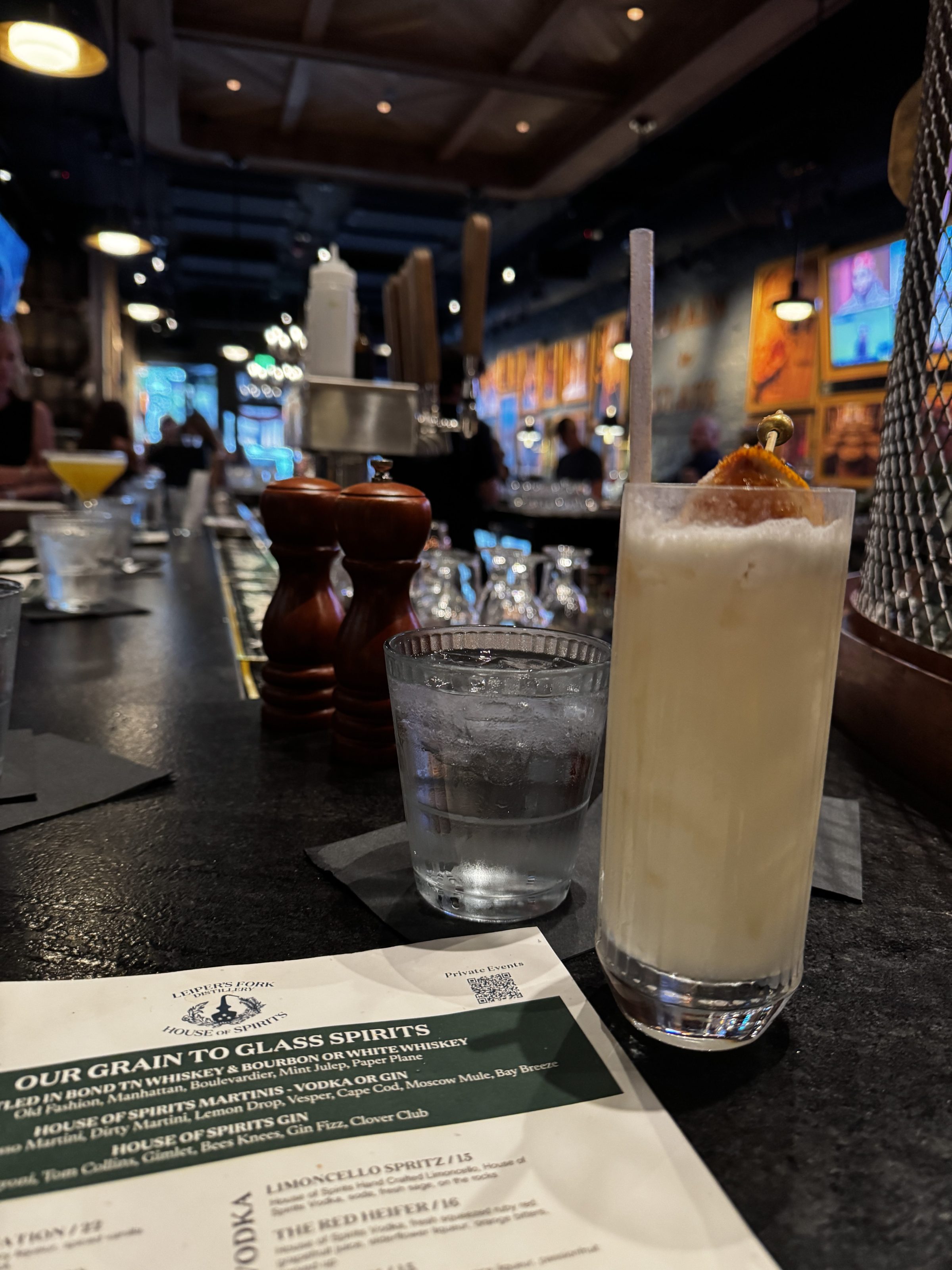 Iced cocktail and glass of water on a bar with a menu nearby.