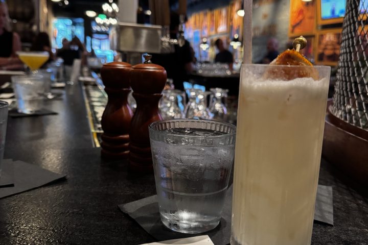 Iced cocktail and glass of water on a bar with a menu nearby.