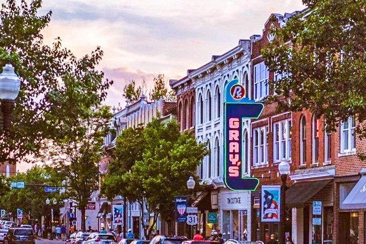 Lively street with historic buildings, trees, and 'Gray's' neon sign at sunset.