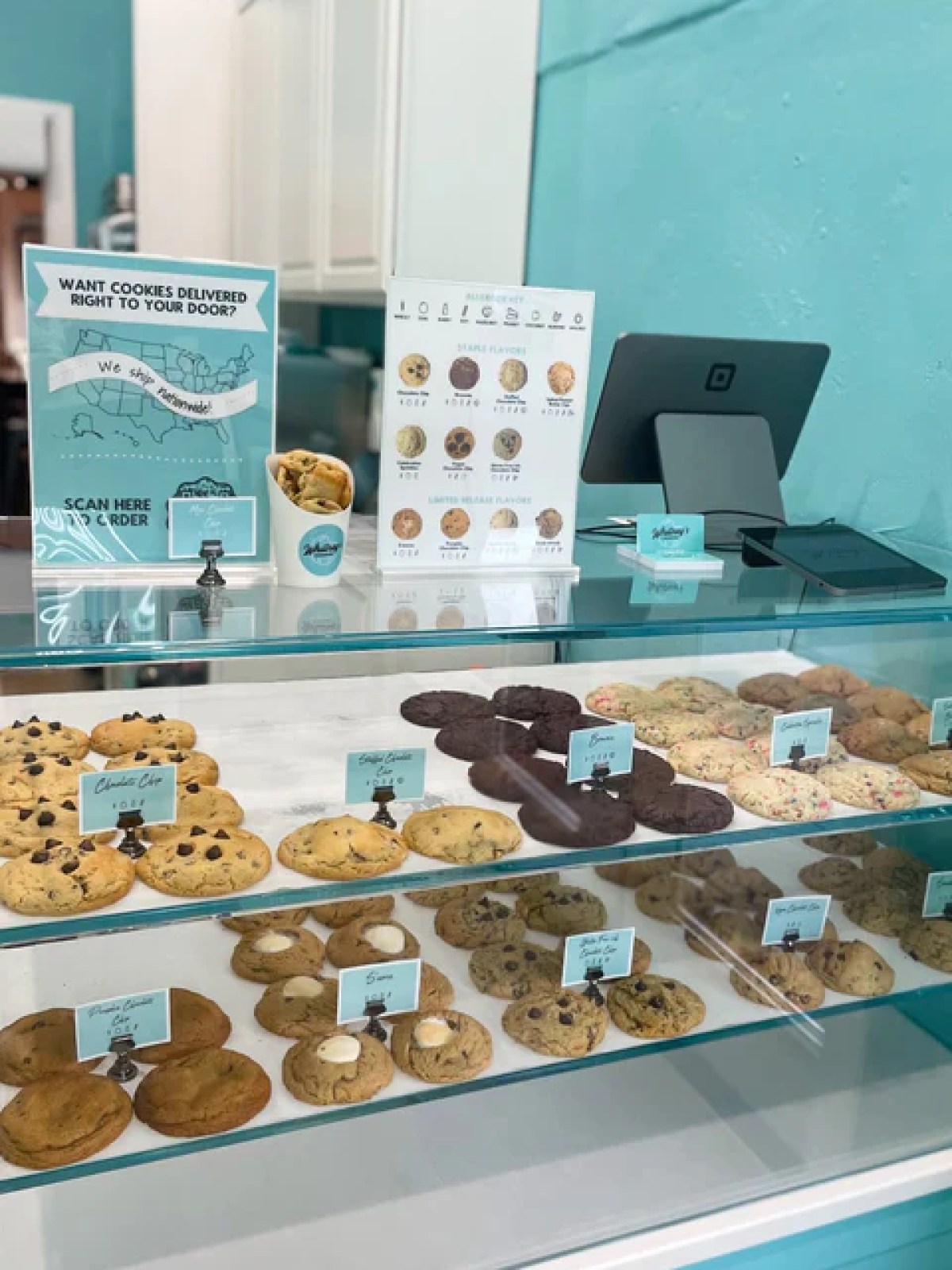 Bakery display with assorted cookies on three shelves in a blue-themed shop.