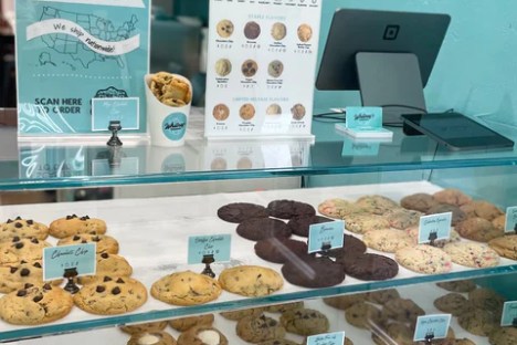 Bakery display with assorted cookies on three shelves in a blue-themed shop.